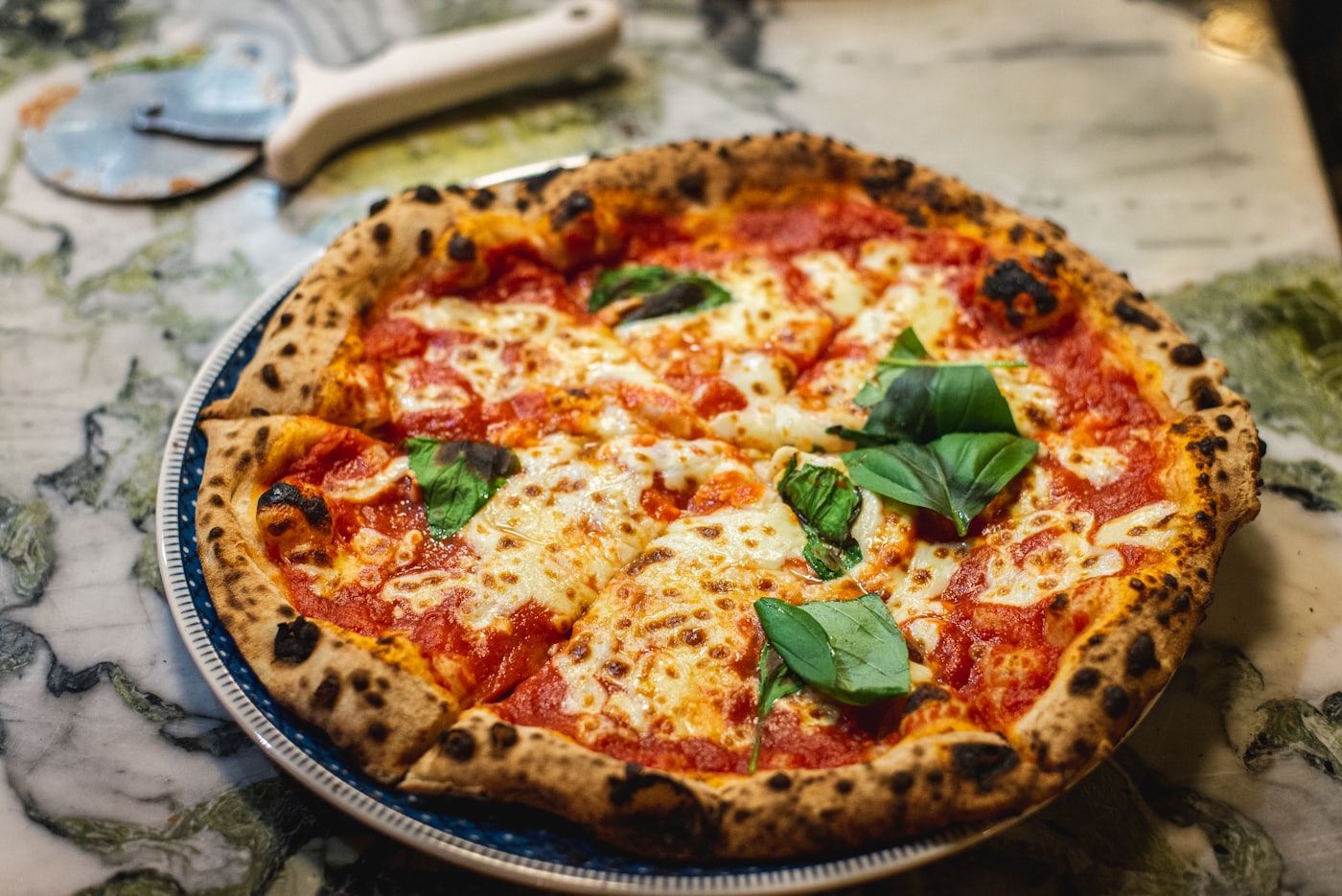 Margherita entière au basilic frais, servie sur une table de marbre clair