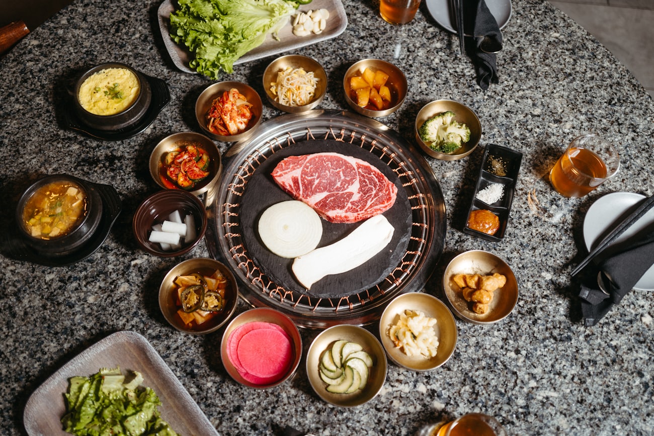 La table vue du dessus : le grill au charbon encastré au centre, entouré de bols de laiton remplis de banchan, sur le granit sombre